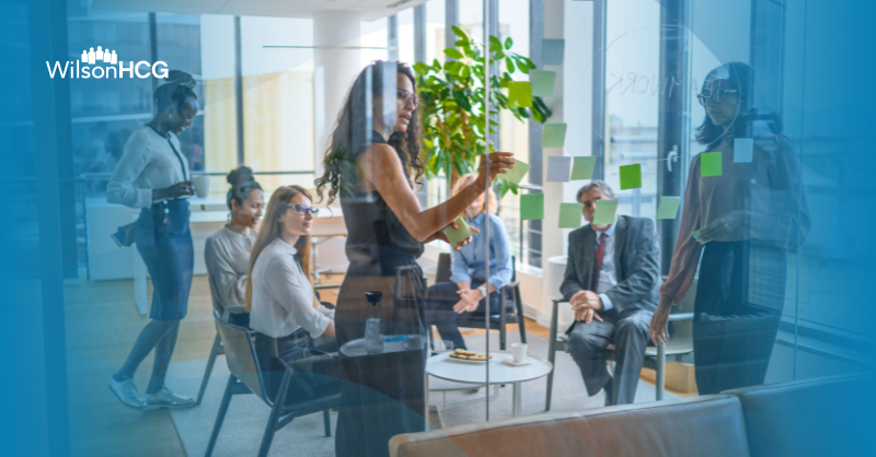 Group of office workers in a meeting discussing strategy with sticky notes on a glass wall