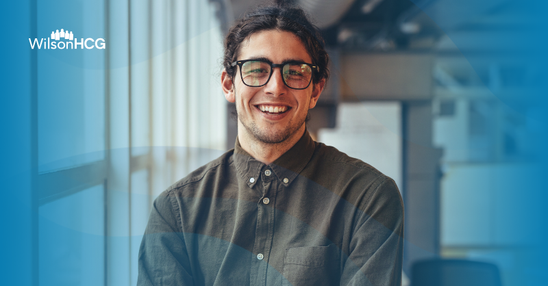 Man smiling at the camera wearing a button up long-sleeve shirt