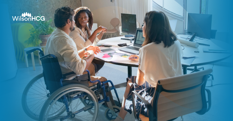 Male business professional in wheelchair talks to two female colleagues.