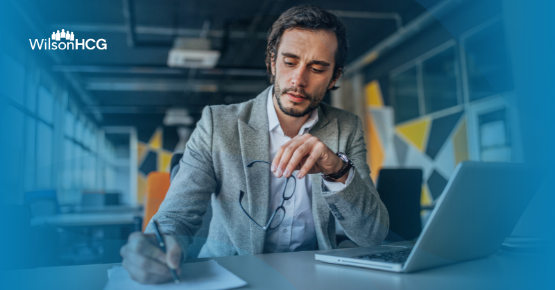 Businessman taking notes while reading an article about AI on his laptop.